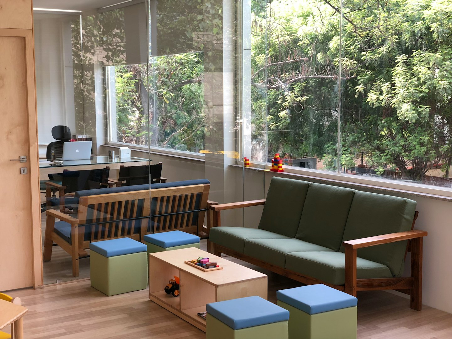 Lounge moderna da ufficio con mobili in legno chiaro e cuscini verdi.